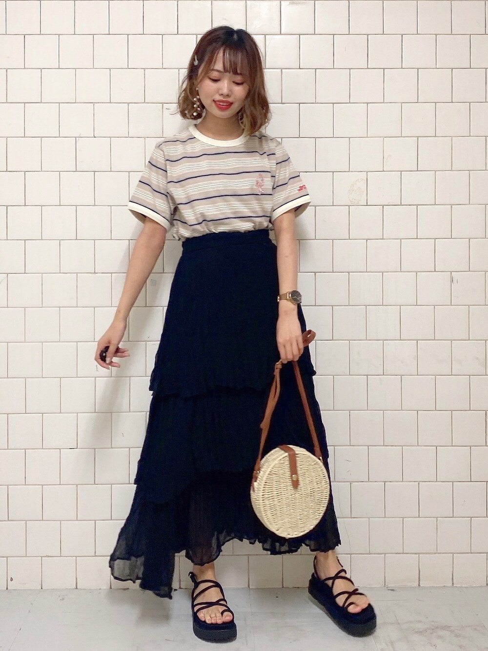 ブラック系のスカート、ベージュ系のTシャツ/カットソー、ブラック系のサンダルを着用したレディースの春コーディネートの1枚目の写真