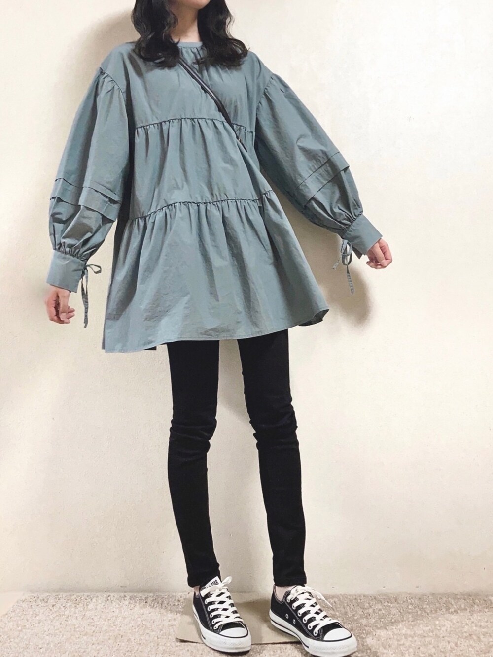 ブルー系のチュニック、ブラック系のパンツ、ブラック系のスニーカーを着用したレディースの春コーディネートの1枚目の写真