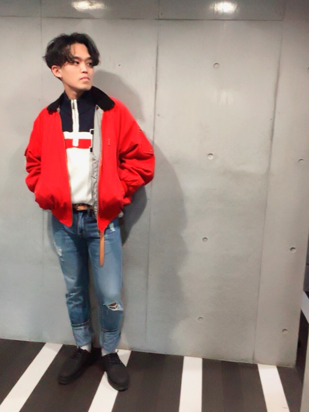 レッド系のブルゾン、ホワイト系のニット/セーター、ブルー系のデニムパンツを着用したメンズの秋コーディネートの1枚目の写真