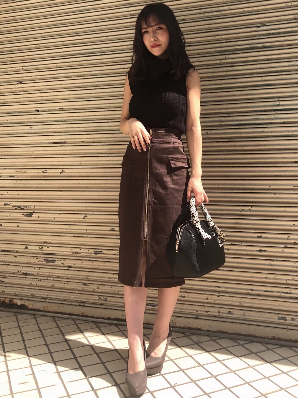 ブラック系のニット/セーター、ブラウン系のスカート、ベージュ系のパンプスを着用したレディースの秋コーディネートの1枚目の写真