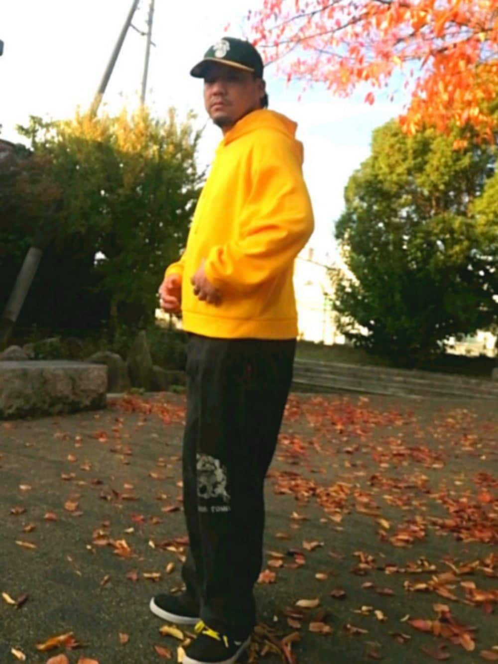 ゴールド系のパーカー、ブラック系のデニムパンツ、ブラック系のスニーカーを着用したメンズの秋コーディネートの1枚目の写真