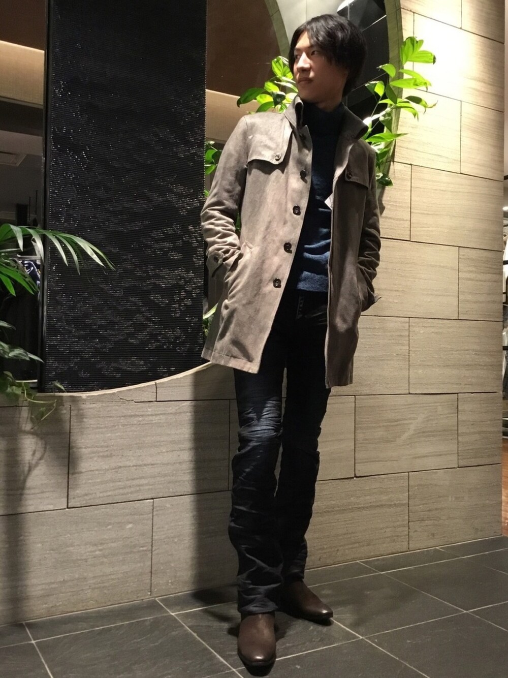 グレー系のステンカラーコート、グリーン系のニット/セーター、ブラック系のその他パンツを着用したメンズの冬コーディネートの1枚目の写真