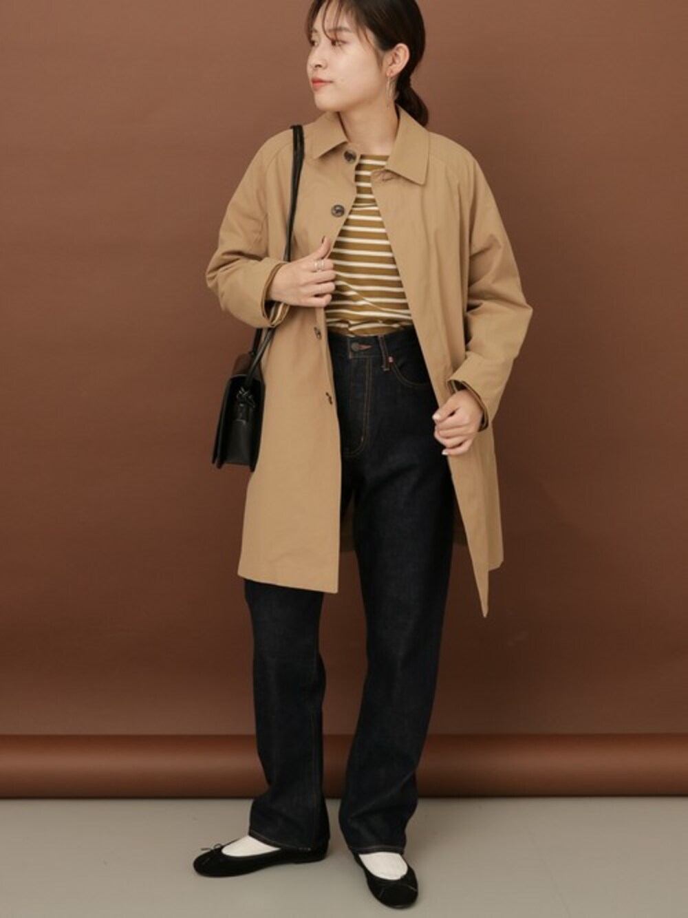 ベージュ系のステンカラーコート、グリーン系のTシャツ/カットソー、ブルー系のデニムパンツを着用したレディースの秋コーディネートの1枚目の写真