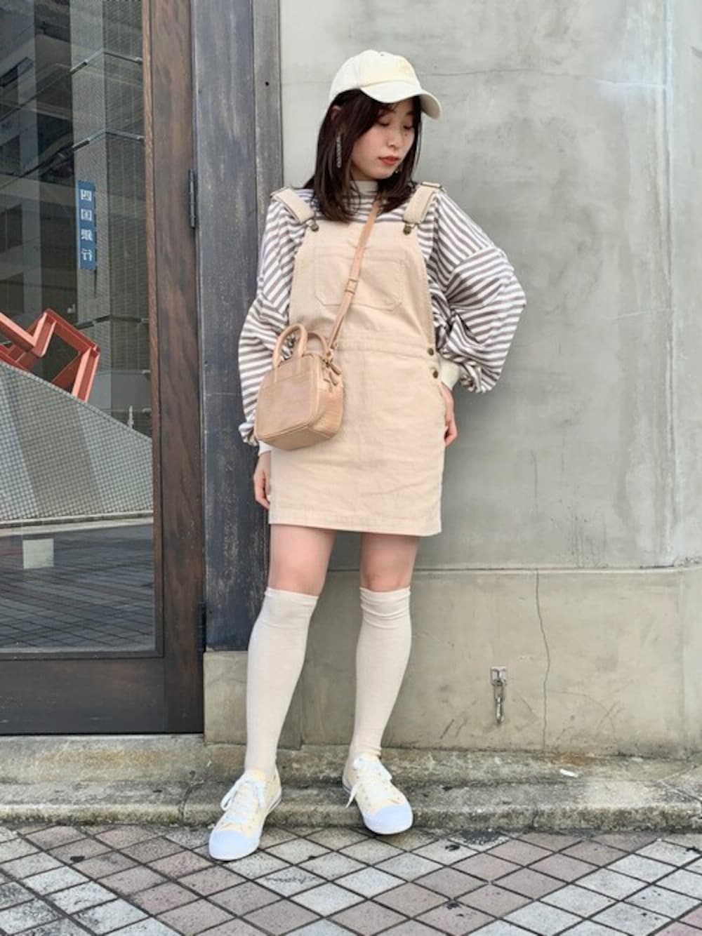 ベージュ系のTシャツ/カットソー、ホワイト系のジャンパースカート、ベージュ系のショルダーバッグを着用したレディースの秋コーディネートの1枚目の写真