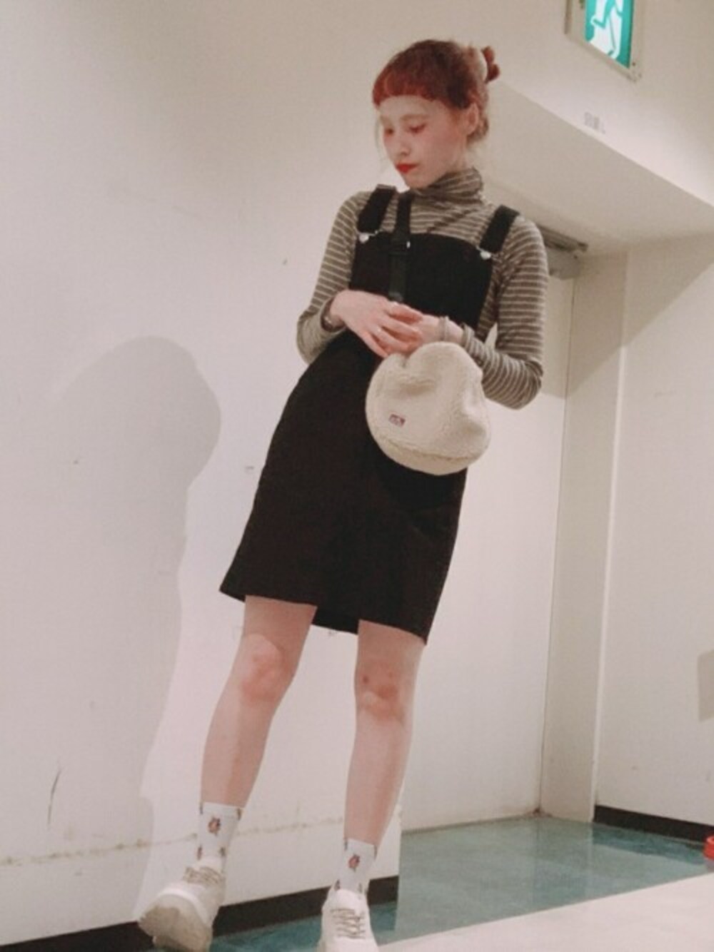 ベージュ系のスニーカー、ベージュ系のショルダーバッグ、ブラック系のジャンパースカートを着用したレディースの秋コーディネートの1枚目の写真