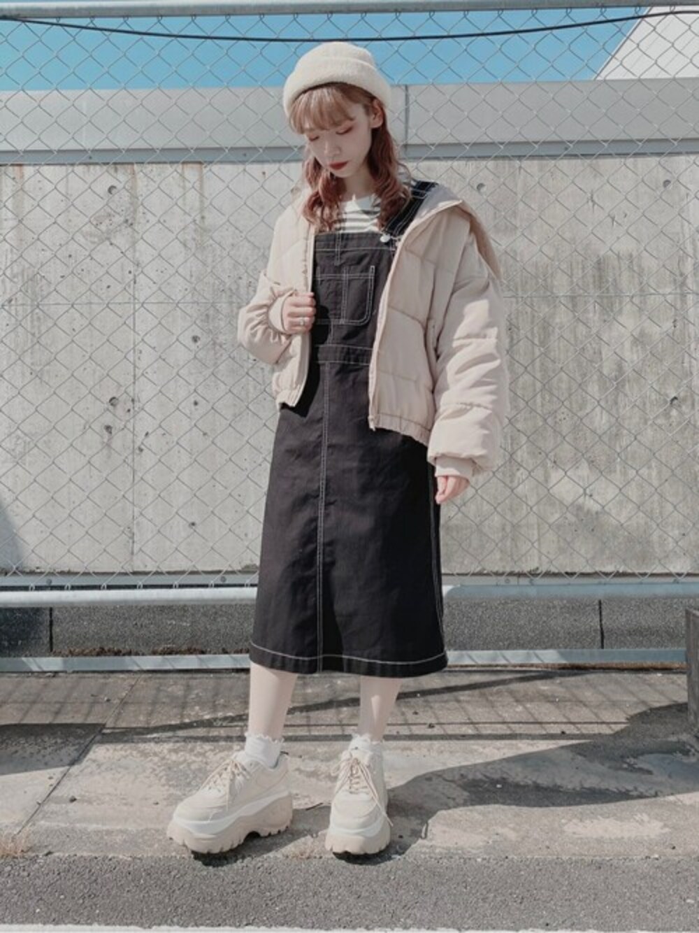 グリーン系のTシャツ/カットソー、ブラック系のジャンパースカート、ベージュ系のダウンジャケット/コートを着用したレディースの秋コーディネートの1枚目の写真