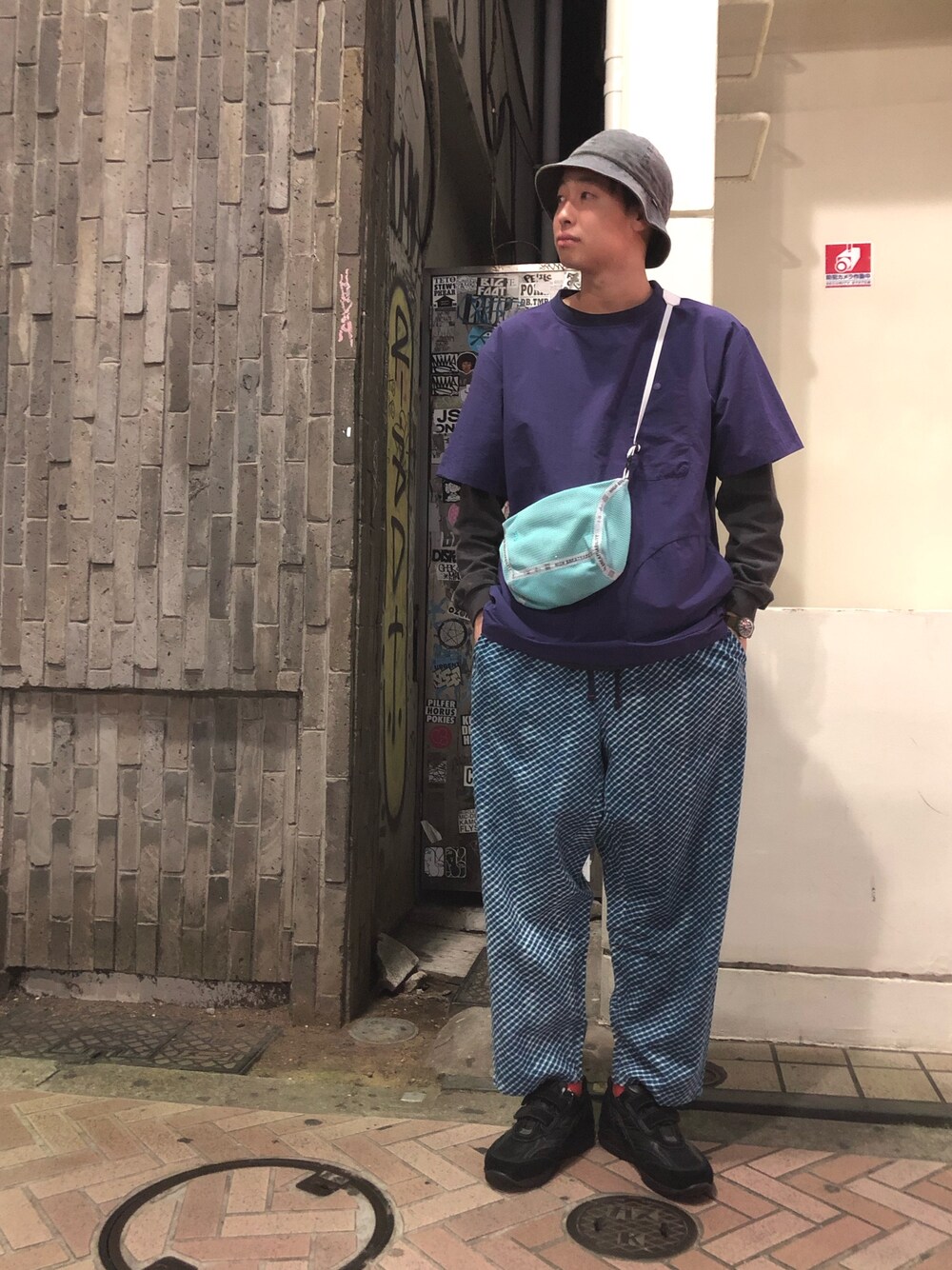 ブラック系のスニーカー、ブルー系のショルダーバッグ、ベージュ系のTシャツ/カットソーを着用したメンズの春コーディネートの1枚目の写真