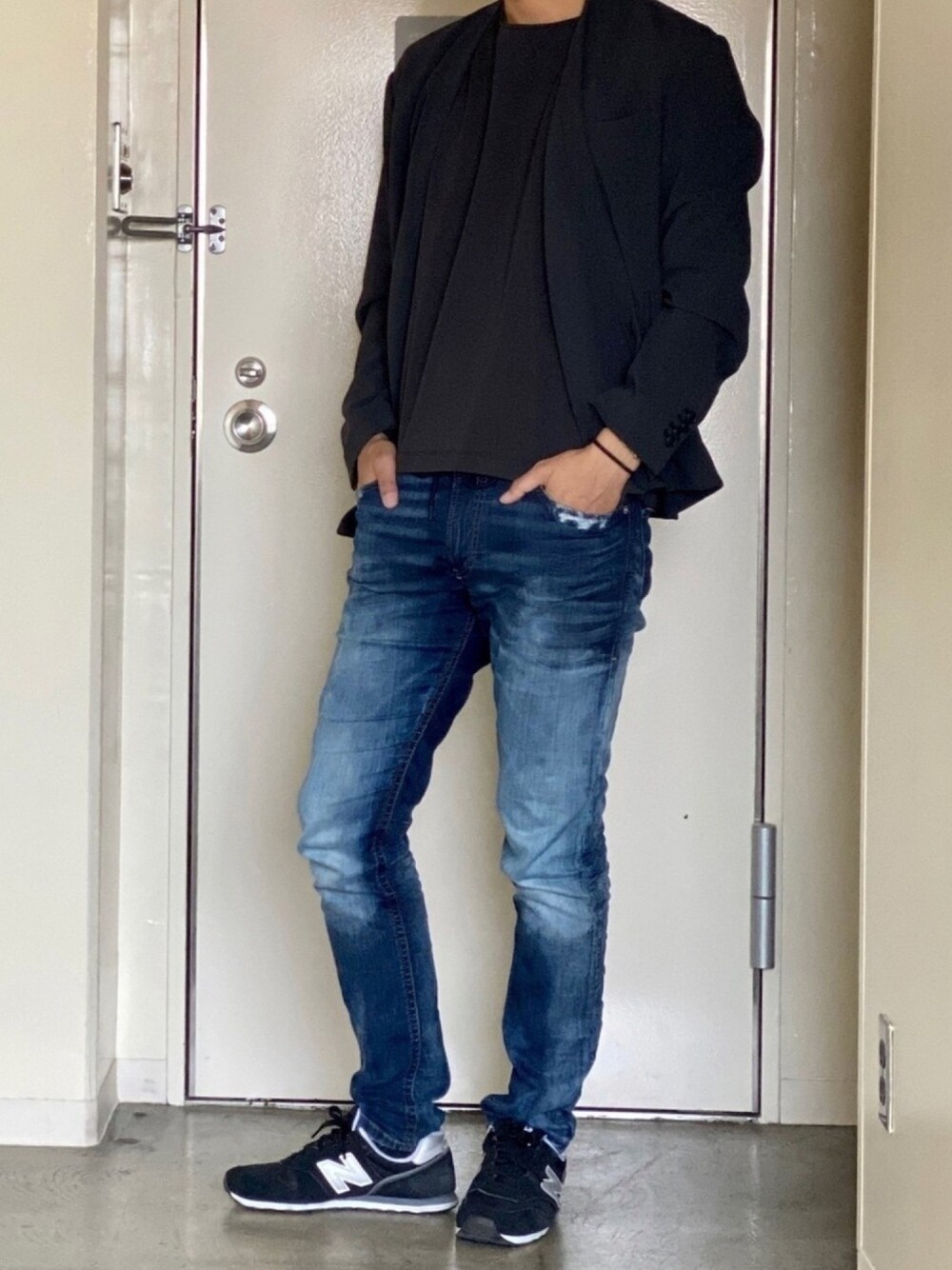 ブラック系のノーカラージャケット、ブラック系のTシャツ/カットソー、ブルー系のデニムパンツを着用したメンズの春コーディネートの1枚目の写真