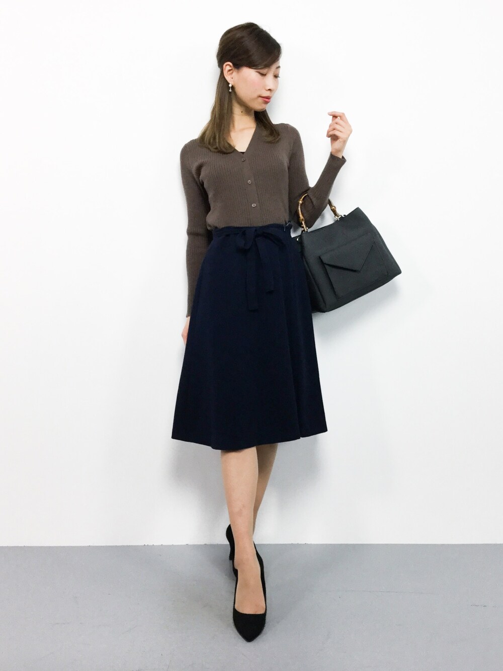 ブラウン系のカーディガン/ボレロ、ブラック系のトートバッグ、ブルー系のスカートを着用したレディースの秋コーディネートの1枚目の写真