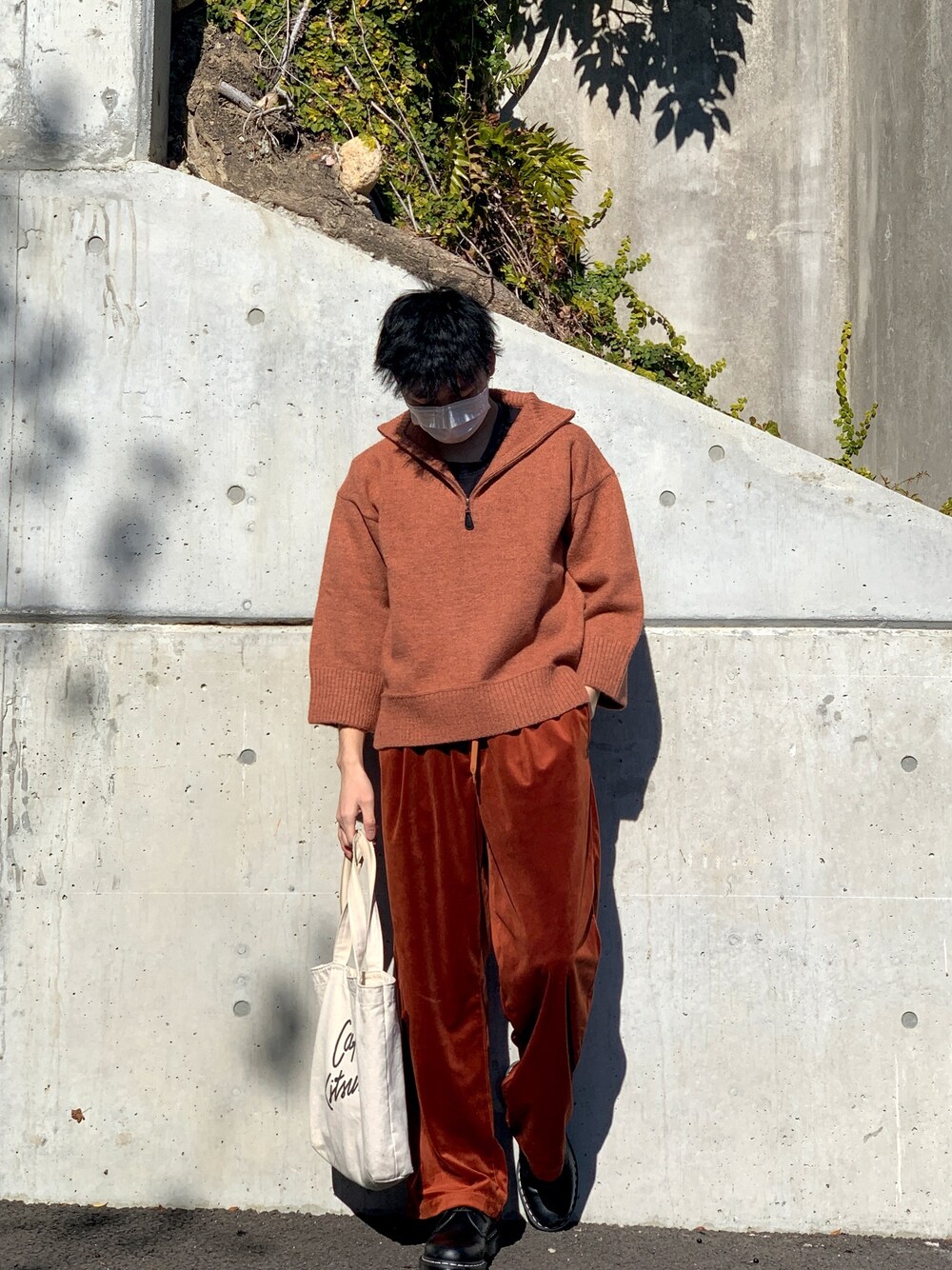 オレンジ系のニット/セーター、レッド系のその他パンツ、ベージュ系のトートバッグを着用したメンズの冬コーディネートの1枚目の写真