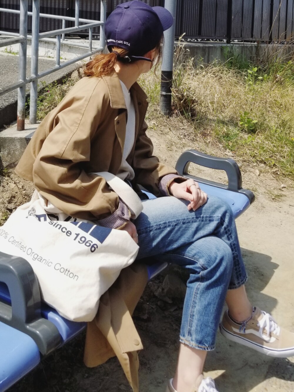 ブルー系のトートバッグ、ベージュ系のステンカラーコート、ホワイト系のTシャツ/カットソーを着用したレディースの春コーディネートの1枚目の写真