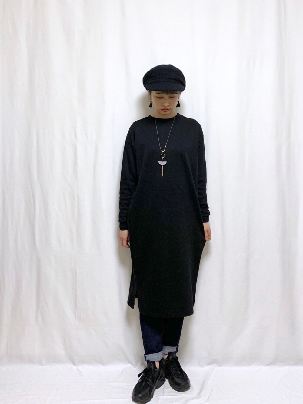 ブラック系のワンピース、ブルー系のデニムパンツ、ブラック系のスニーカーを着用したレディースの冬コーディネートの1枚目の写真