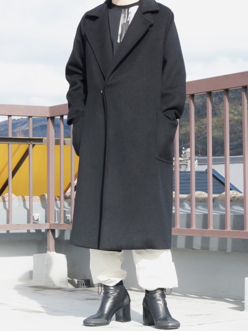 ブラック系のTシャツ/カットソー、ブラック系のチェスターコート、ブラック系のブーツを着用したメンズの冬コーディネートの1枚目の写真