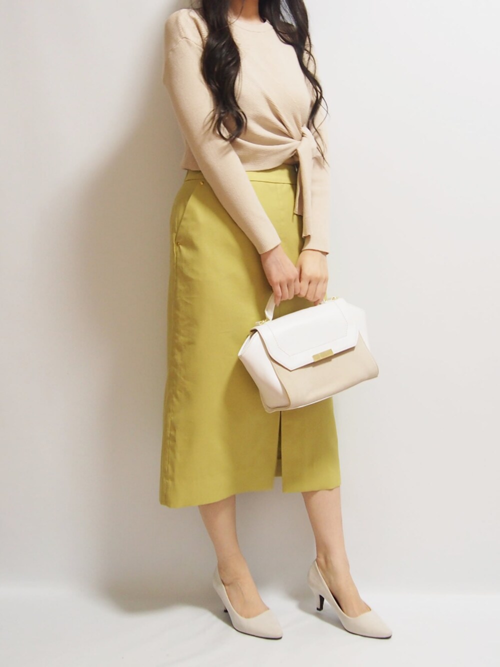 イエロー系のスカート、ホワイト系のパンプス、ベージュ系のニット/セーターを着用したレディースの春コーディネートの1枚目の写真