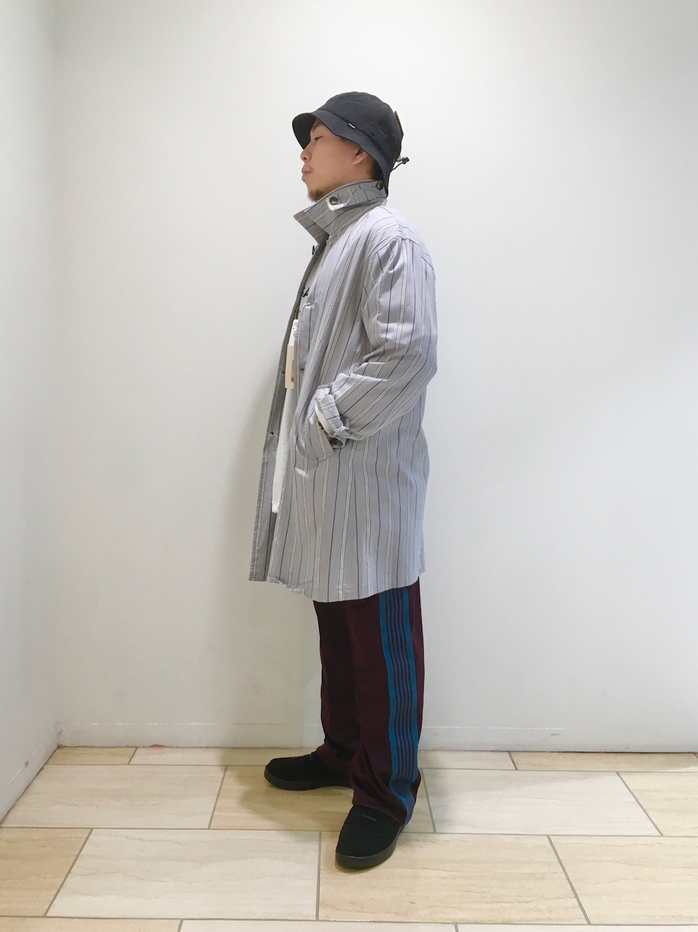 グレー系のステンカラーコート、ブラック系のスニーカー、ブラック系のハットを着用したメンズの春コーディネートの1枚目の写真