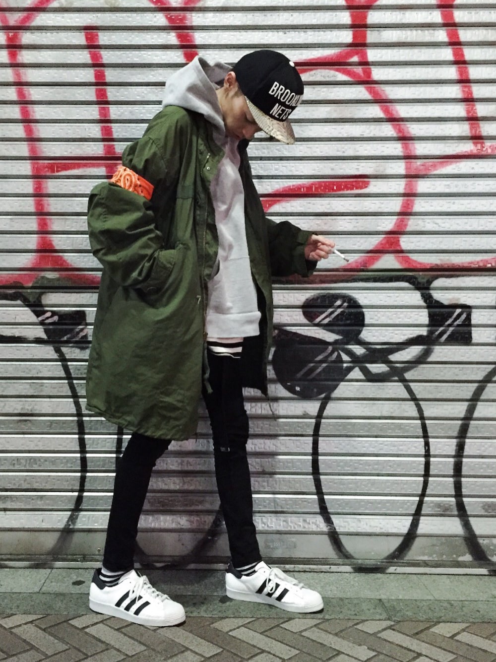 グリーン系のミリタリージャケット、ホワイト系のスニーカー、ブラック系のキャップを着用したメンズの春コーディネートの1枚目の写真
