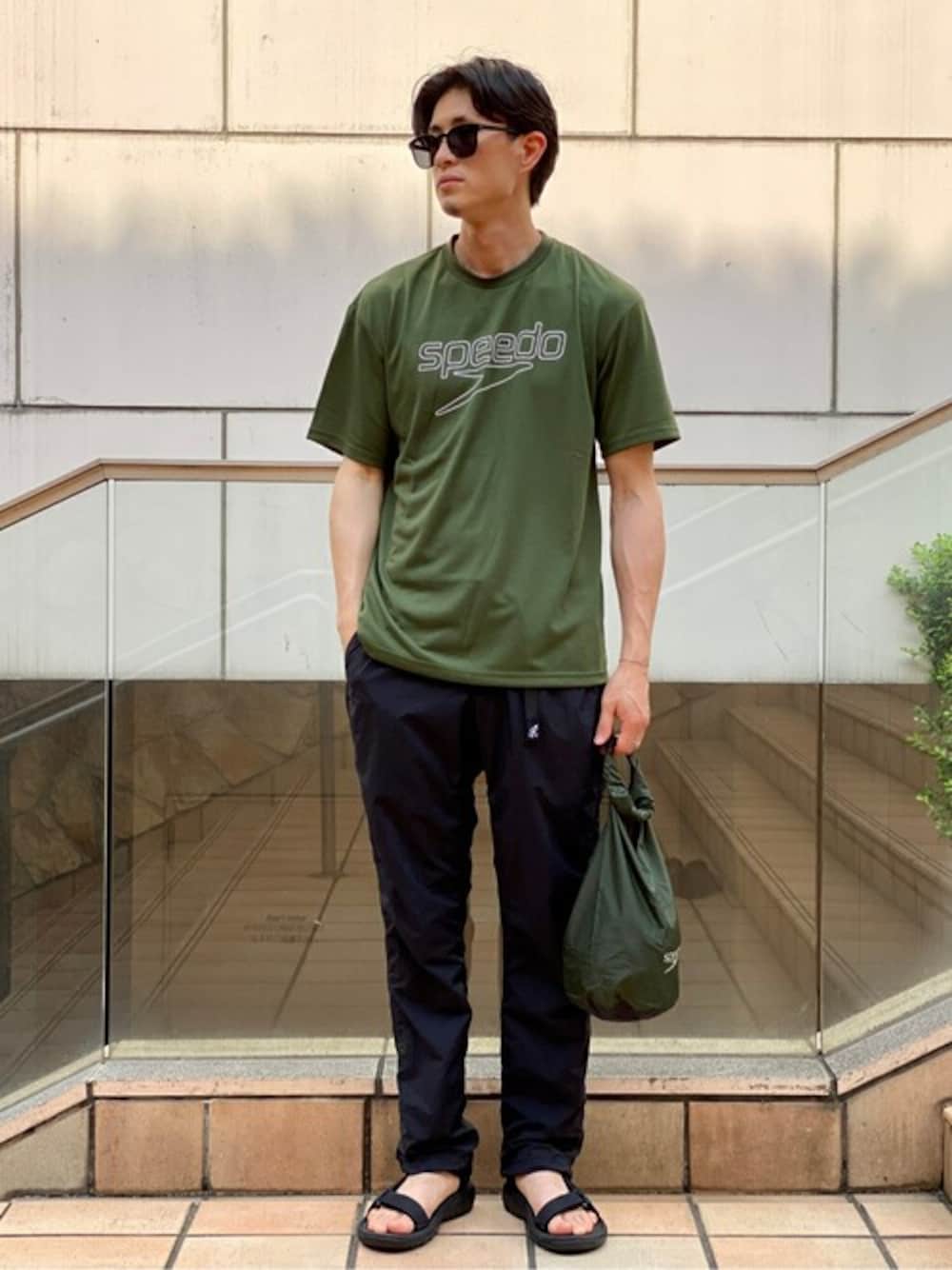 グリーン系のTシャツ/カットソー、ブラック系のサンダル、ブラック系のエコバッグ/サブバッグを着用したメンズの夏コーディネートの1枚目の写真