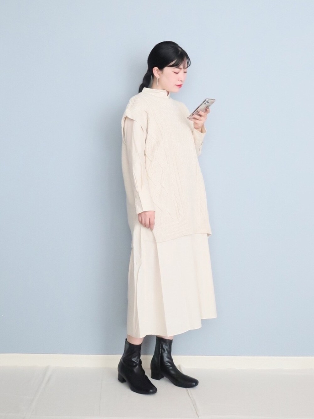 ホワイト系のベスト、ホワイト系のワンピース、ブラック系のブーツを着用したレディースの秋コーディネートの1枚目の写真