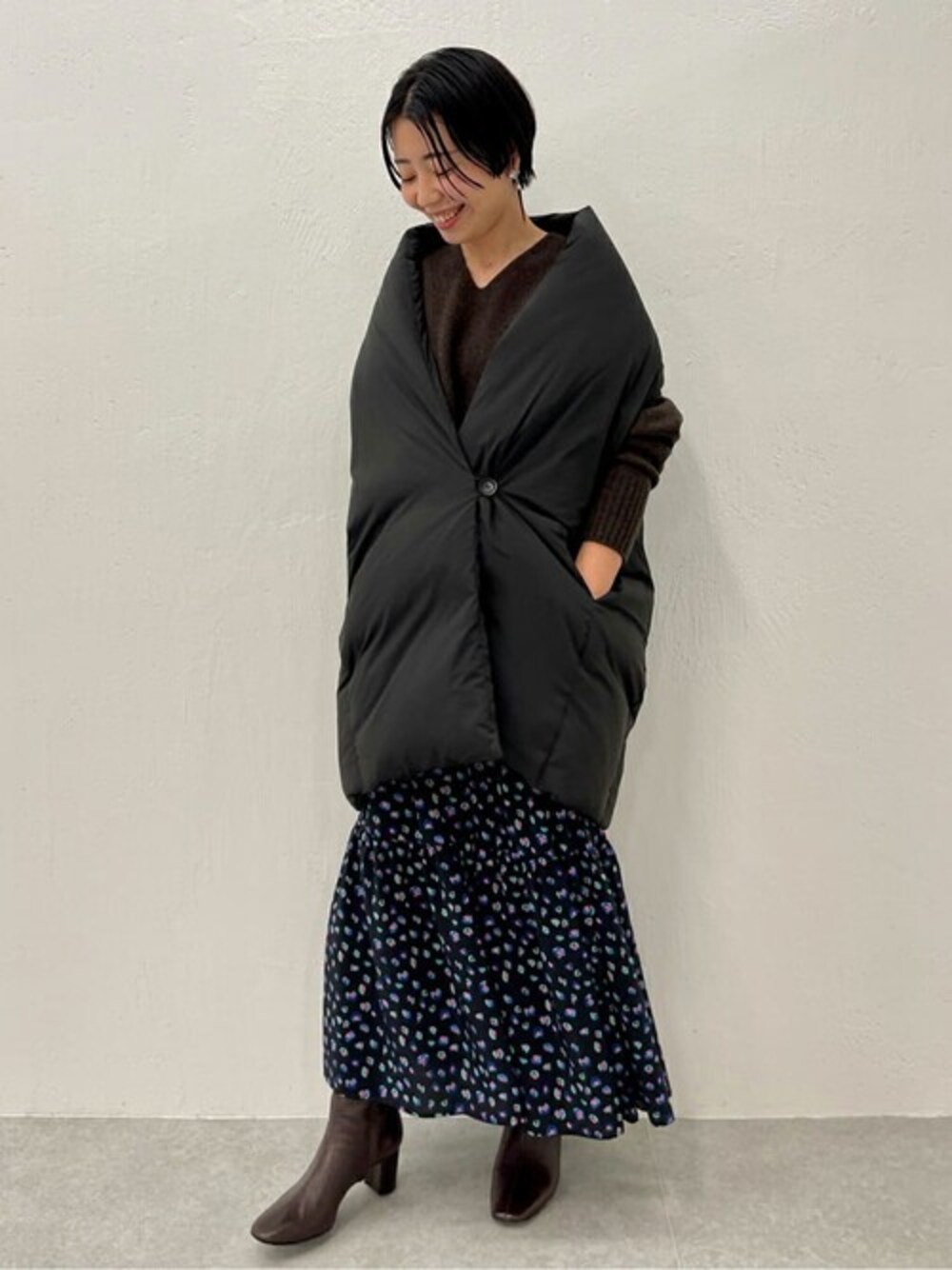 ブラック系のダウンベスト、ブラウン系のニット/セーター、ブラック系のスカートを着用したレディースの秋コーディネートの1枚目の写真