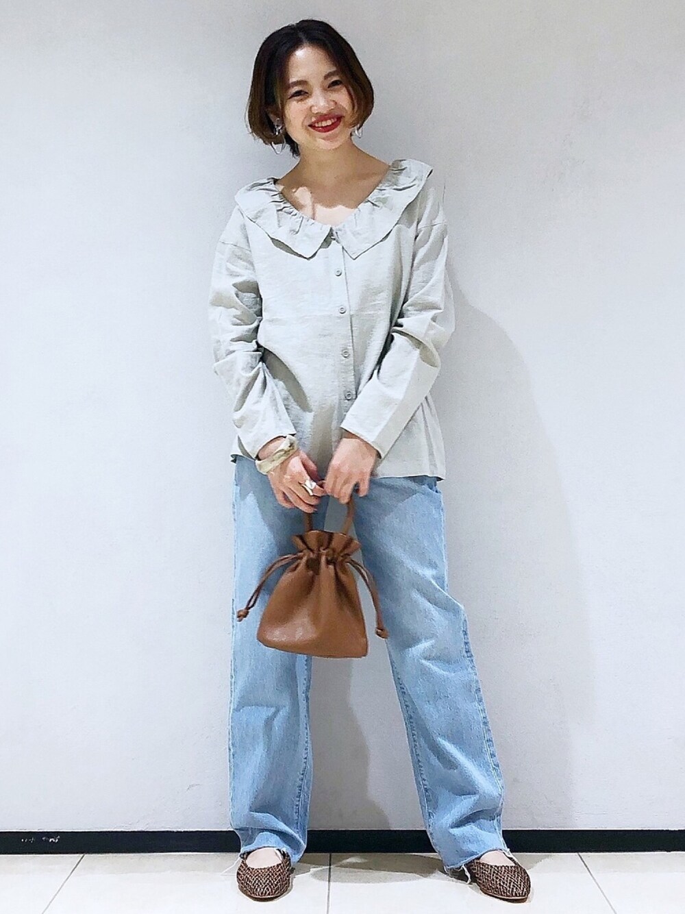 ベージュ系のシャツ/ブラウス、ブラウン系のショルダーバッグ、ブルー系のデニムパンツを着用したレディースの春コーディネートの1枚目の写真