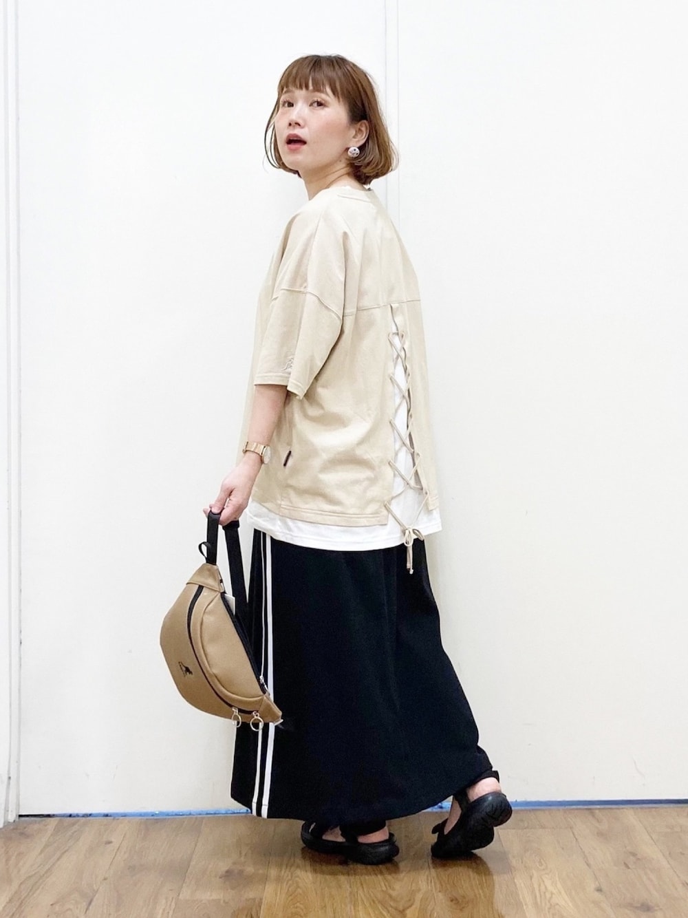ベージュ系のTシャツ/カットソー、ブラック系のスカート、ベージュ系のボディバッグ/ウエストポーチを着用したレディースの春コーディネートの1枚目の写真