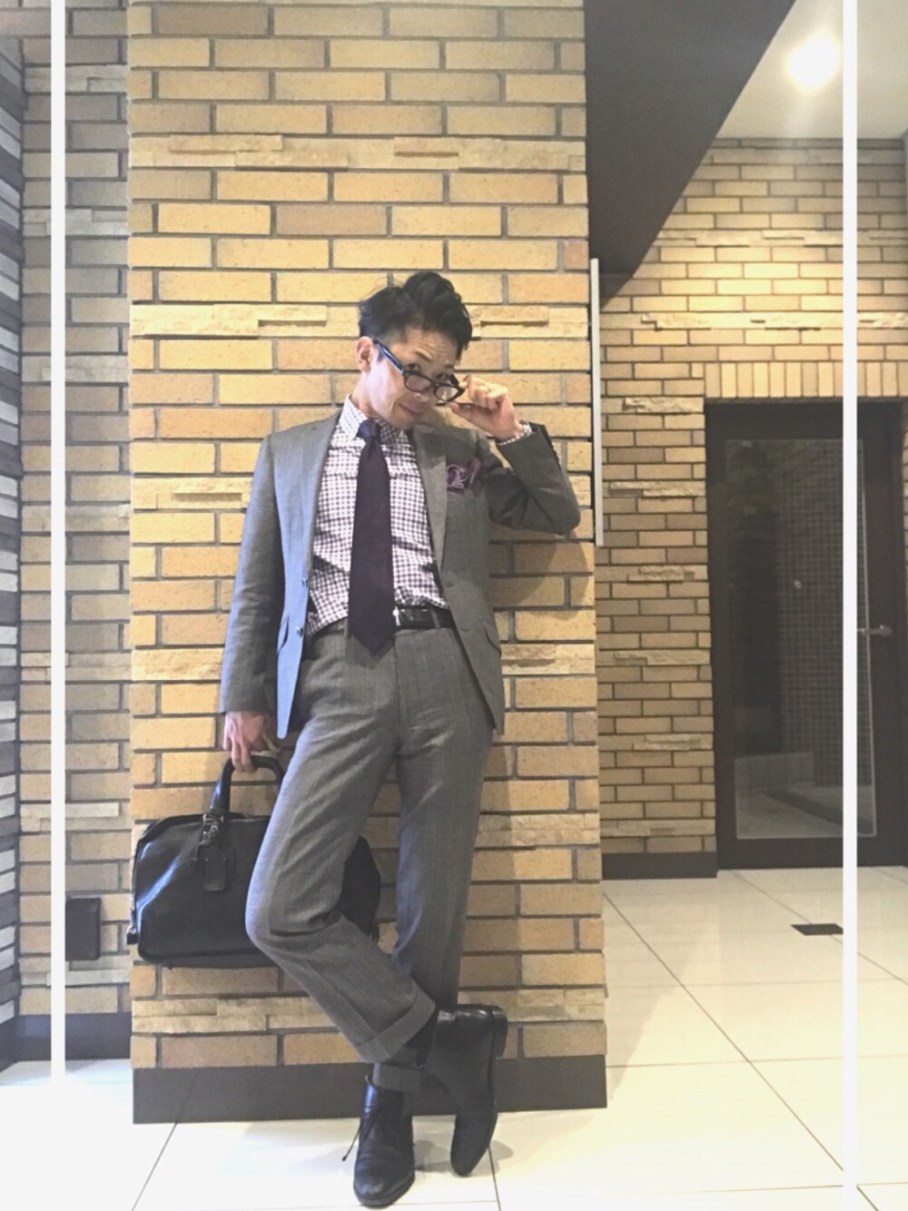 グレー系のスーツジャケット、ブラック系のドレスシューズ、ブラック系のビジネスバッグを着用したメンズの秋コーディネートの1枚目の写真