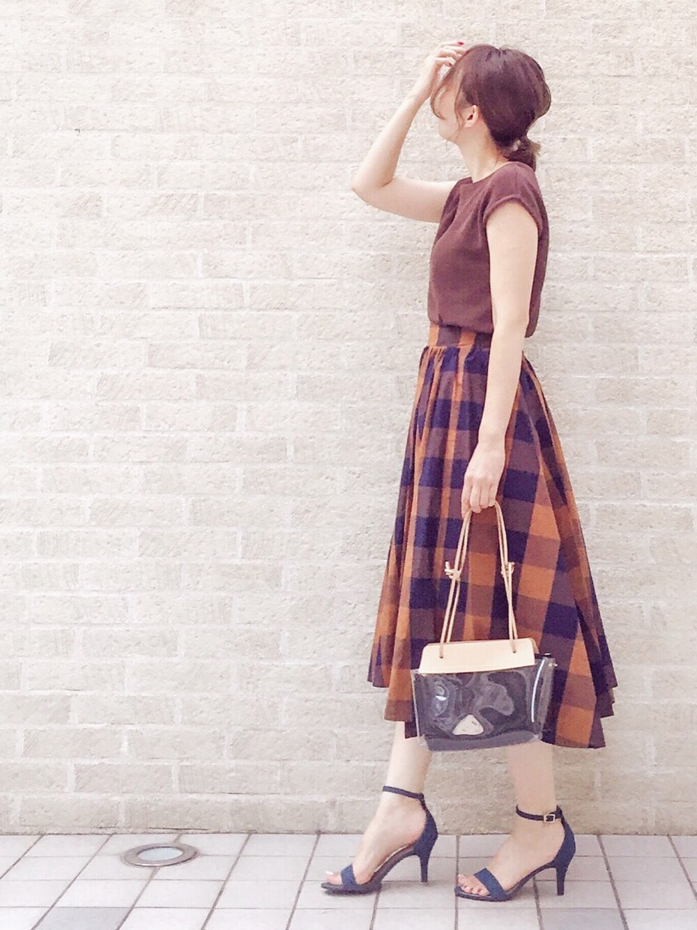 ブラウン系のニット/セーター、ブラウン系のスカート、ブラック系のハンドバッグを着用したレディースの夏コーディネートの1枚目の写真