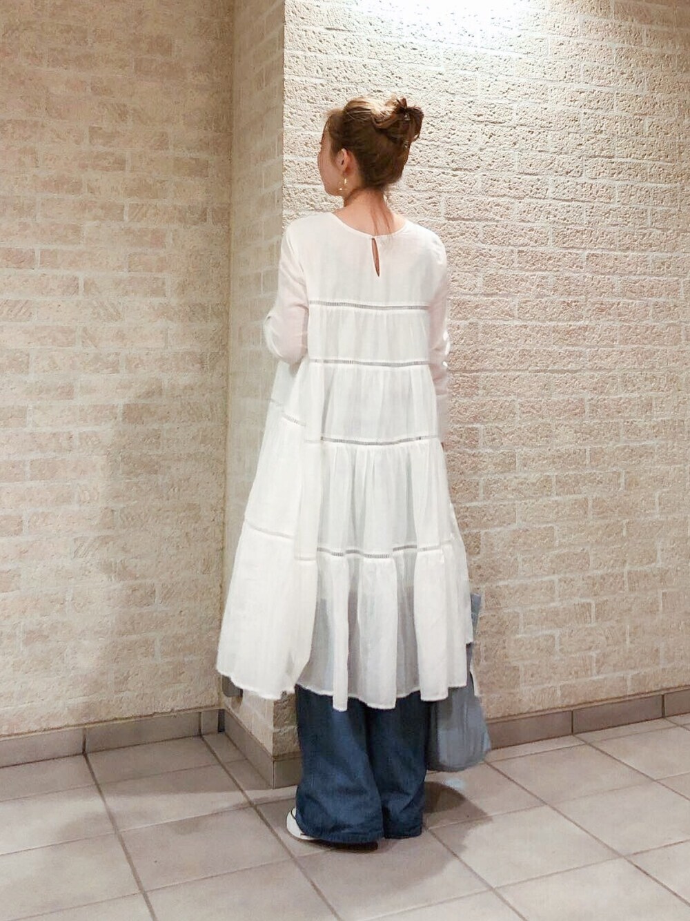 ホワイト系のワンピース、ブルー系のデニムパンツ、ブラウン系のスニーカーを着用したレディースの春コーディネートの1枚目の写真