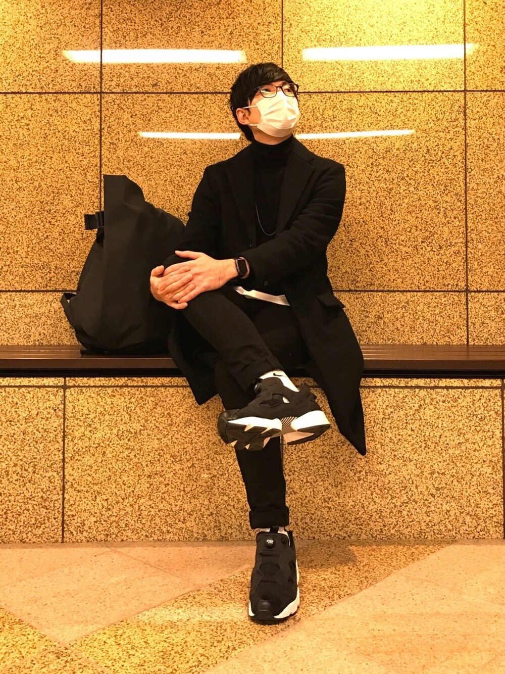 ブラック系のチェスターコート、ブラック系のニット/セーター、ホワイト系のTシャツ/カットソーを着用したメンズの冬コーディネートの1枚目の写真