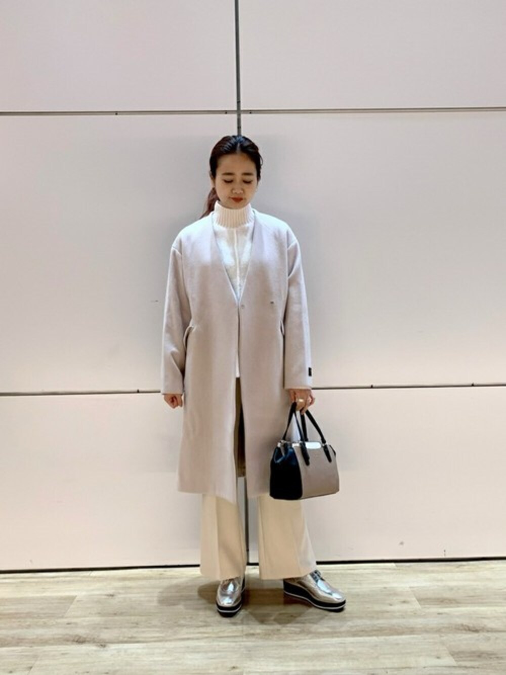 シルバー系のドレスシューズ、ベージュ系のトートバッグ、ベージュ系のノーカラーコートを着用したレディースの冬コーディネートの1枚目の写真