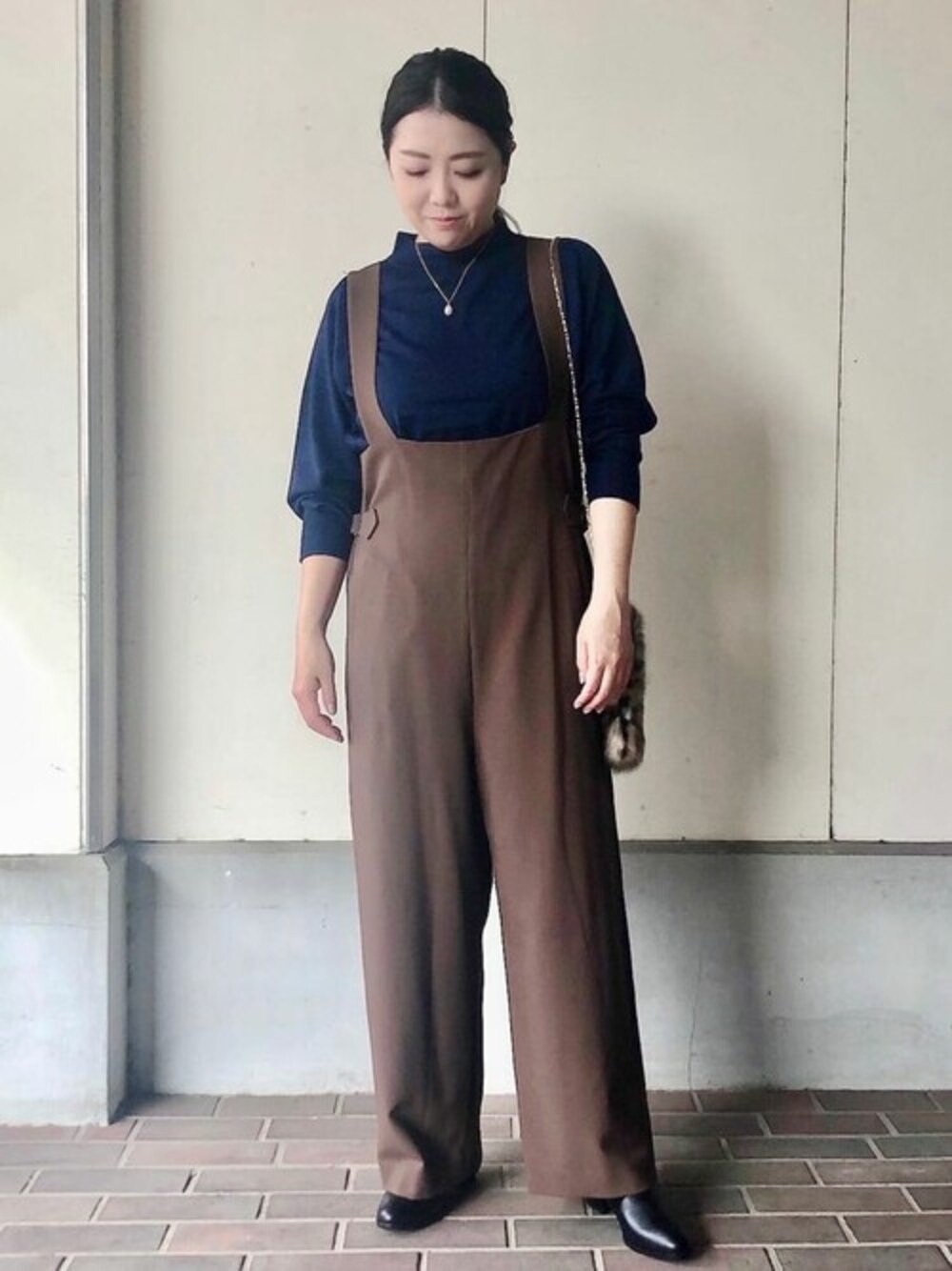 ブルー系のニット/セーター、ベージュ系のサロペット/オーバーオール、ベージュ系のハンドバッグを着用したレディースの秋コーディネートの1枚目の写真