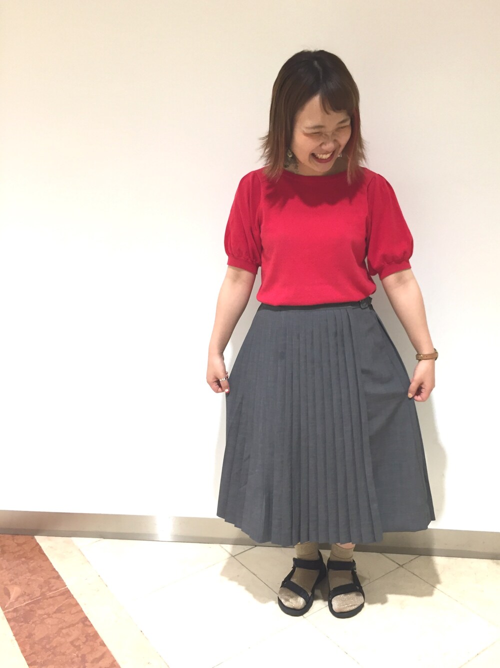 レッド系のニット/セーター、グレー系のスカートを着用したレディースの夏コーディネートの1枚目の写真