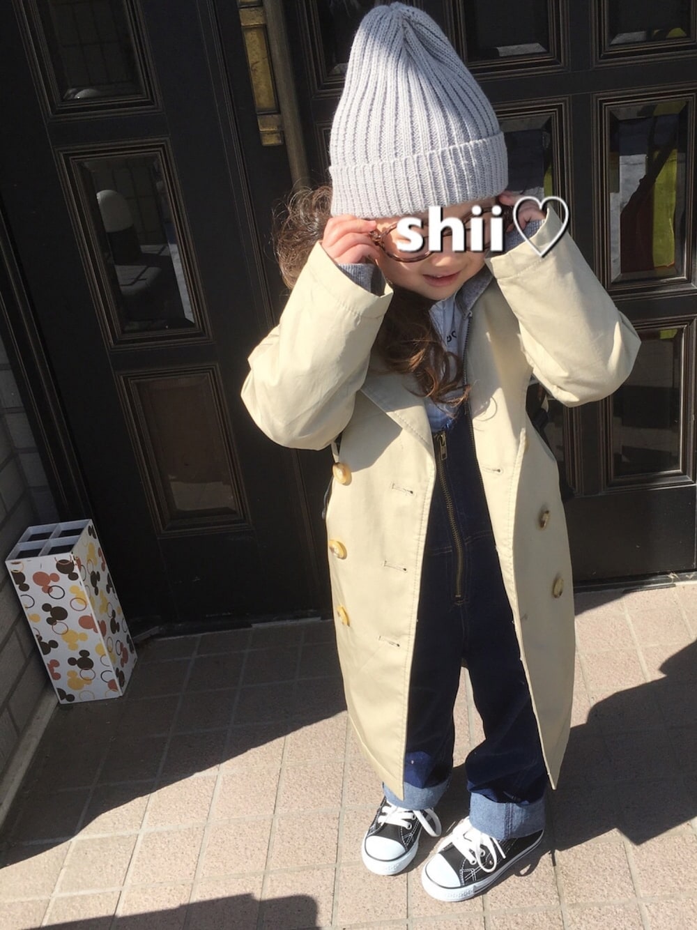 ベージュ系のトレンチコート、ホワイト系のシャツ/ブラウス、ブルー系のサロペット/オーバーオールを着用したキッズの冬コーディネートの1枚目の写真