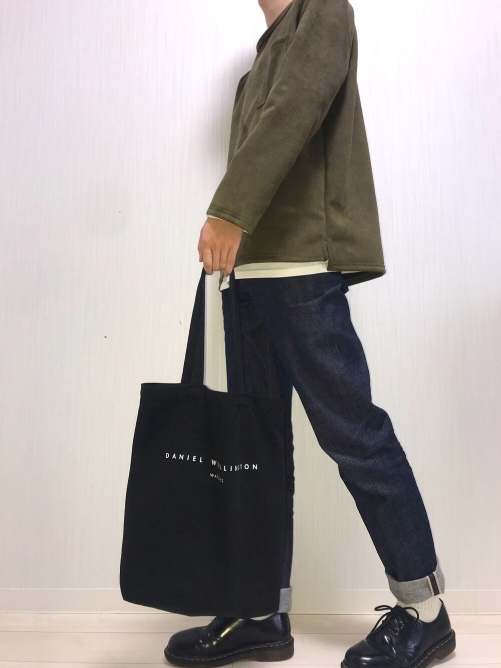ブルー系のデニムパンツ、ブラック系のトートバッグ、ブラック系のブーツを着用したメンズの春コーディネートの1枚目の写真