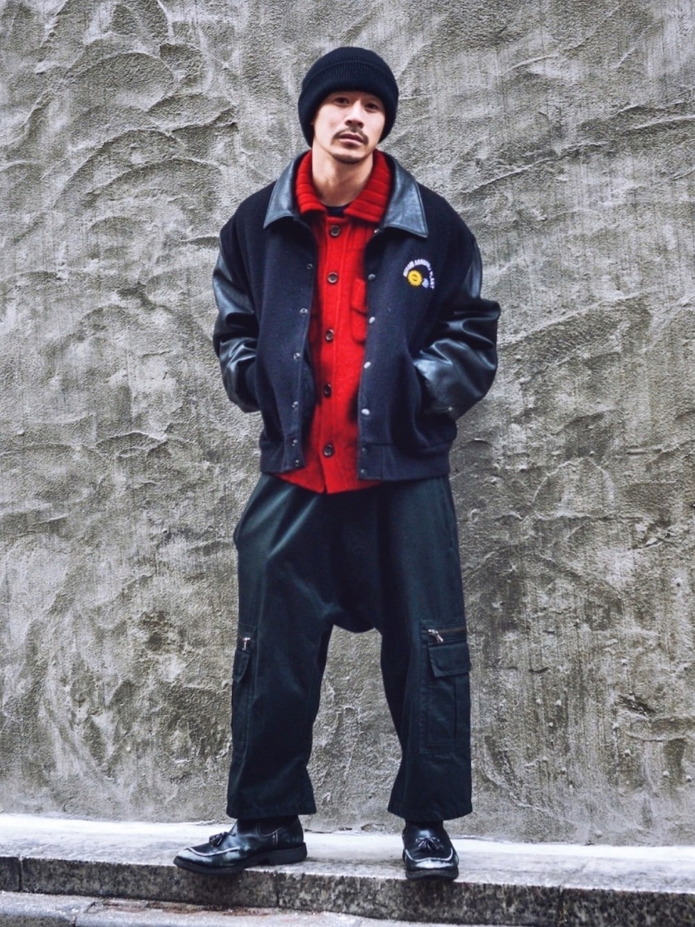 ブラック系のスタジャン、レッド系のニット/セーター、ブラック系のカーゴパンツを着用したメンズの冬コーディネートの1枚目の写真
