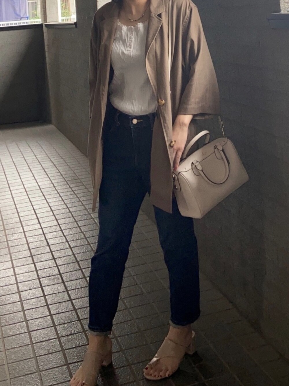 ブルー系のデニムパンツ、ベージュ系のサンダル、ホワイト系のショルダーバッグを着用したレディースの夏コーディネートの1枚目の写真