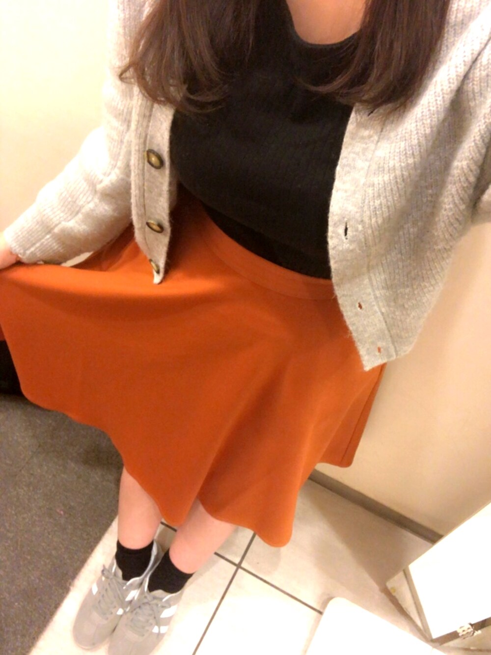 ブラック系のTシャツ/カットソー、グレー系のカーディガン/ボレロ、オレンジ系のスカートを着用したレディースの秋コーディネートの1枚目の写真