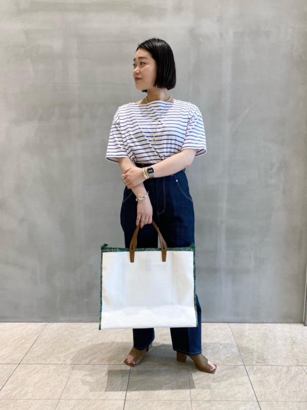 ホワイト系のトートバッグ、ブラウン系のサンダル、ブルー系のTシャツ/カットソーを着用したレディースの夏コーディネートの1枚目の写真