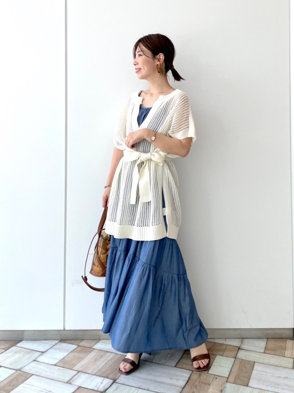 ホワイト系のベスト、ブルー系のワンピース、ブラウン系のサンダルを着用したレディースの春コーディネートの1枚目の写真