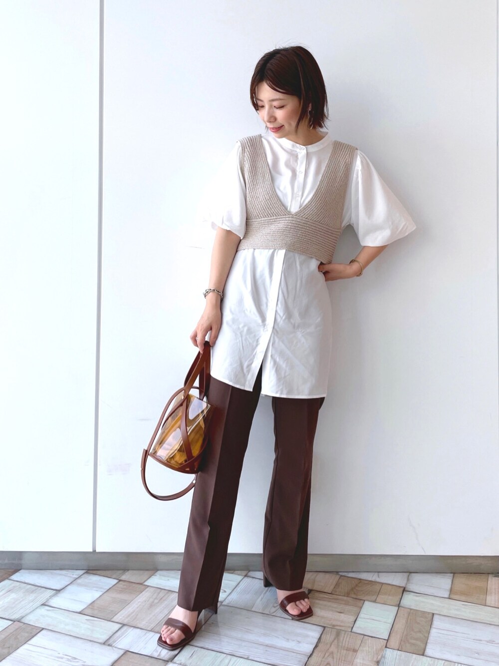 ベージュ系のトップス、ブラウン系のスラックス、イエロー系のショルダーバッグを着用したレディースの夏コーディネートの1枚目の写真