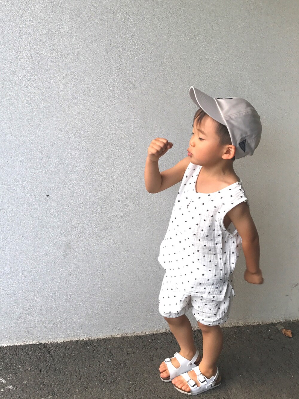 ホワイト系のオールインワン・サロペット、ホワイト系のサンダル、ベージュ系のキャップを着用したレディースの夏コーディネートの1枚目の写真