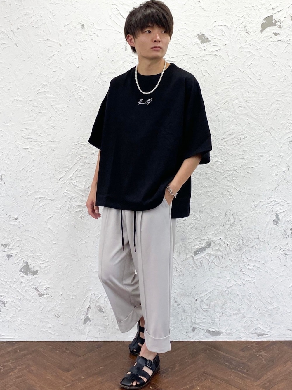 ブラック系のTシャツ/カットソー、グレー系のスラックス、ブラック系のサンダルを着用したメンズの夏コーディネートの1枚目の写真