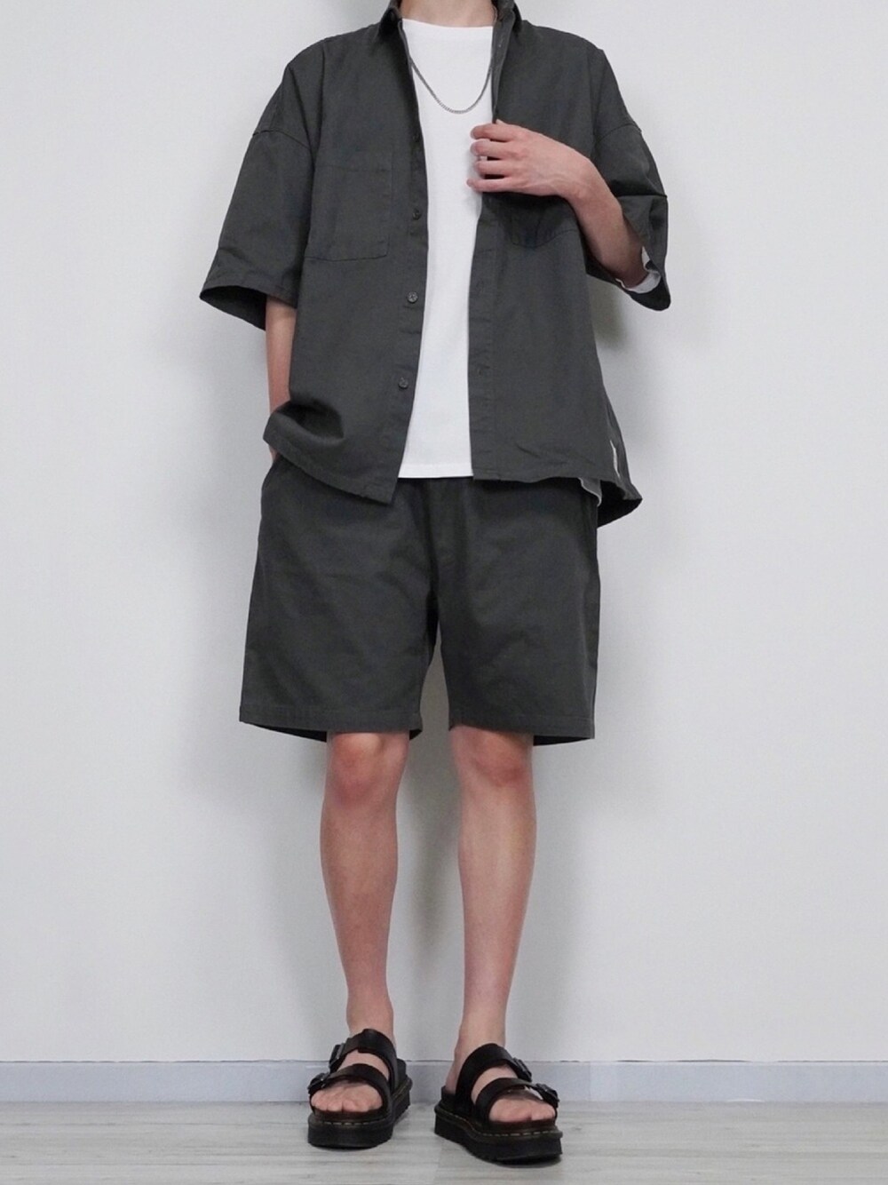 グレー系のセットアップ、ホワイト系のTシャツ/カットソー、ブラック系のサンダルを着用したメンズの夏コーディネートの1枚目の写真