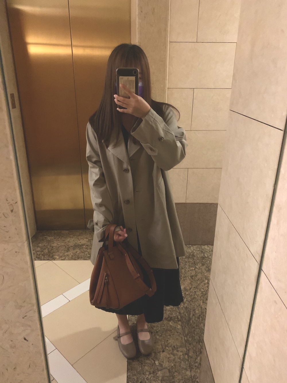 ベージュ系のトレンチコート、ブラウン系のドラムバッグ、ブルー系のワンピースを着用したレディースの春コーディネートの1枚目の写真