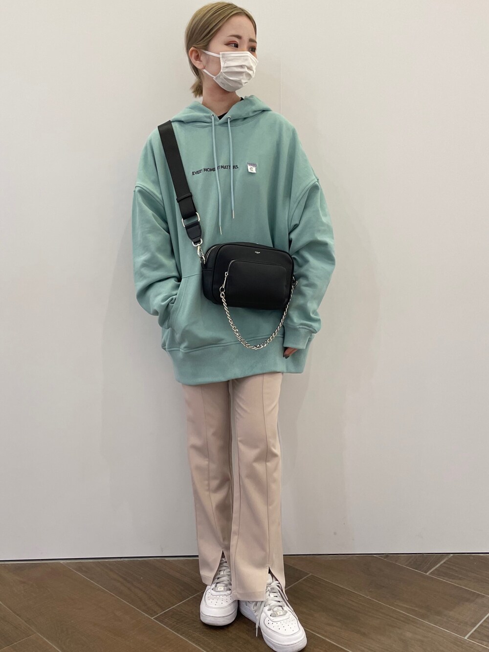 グリーン系のパーカー、ブラック系のショルダーバッグ、ベージュ系のスラックスを着用したレディースの冬コーディネートの1枚目の写真