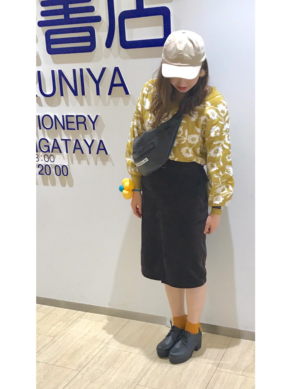 イエロー系のニット/セーター、ブラウン系のスカート、ブラック系のバッグを着用したレディースの秋コーディネートの1枚目の写真