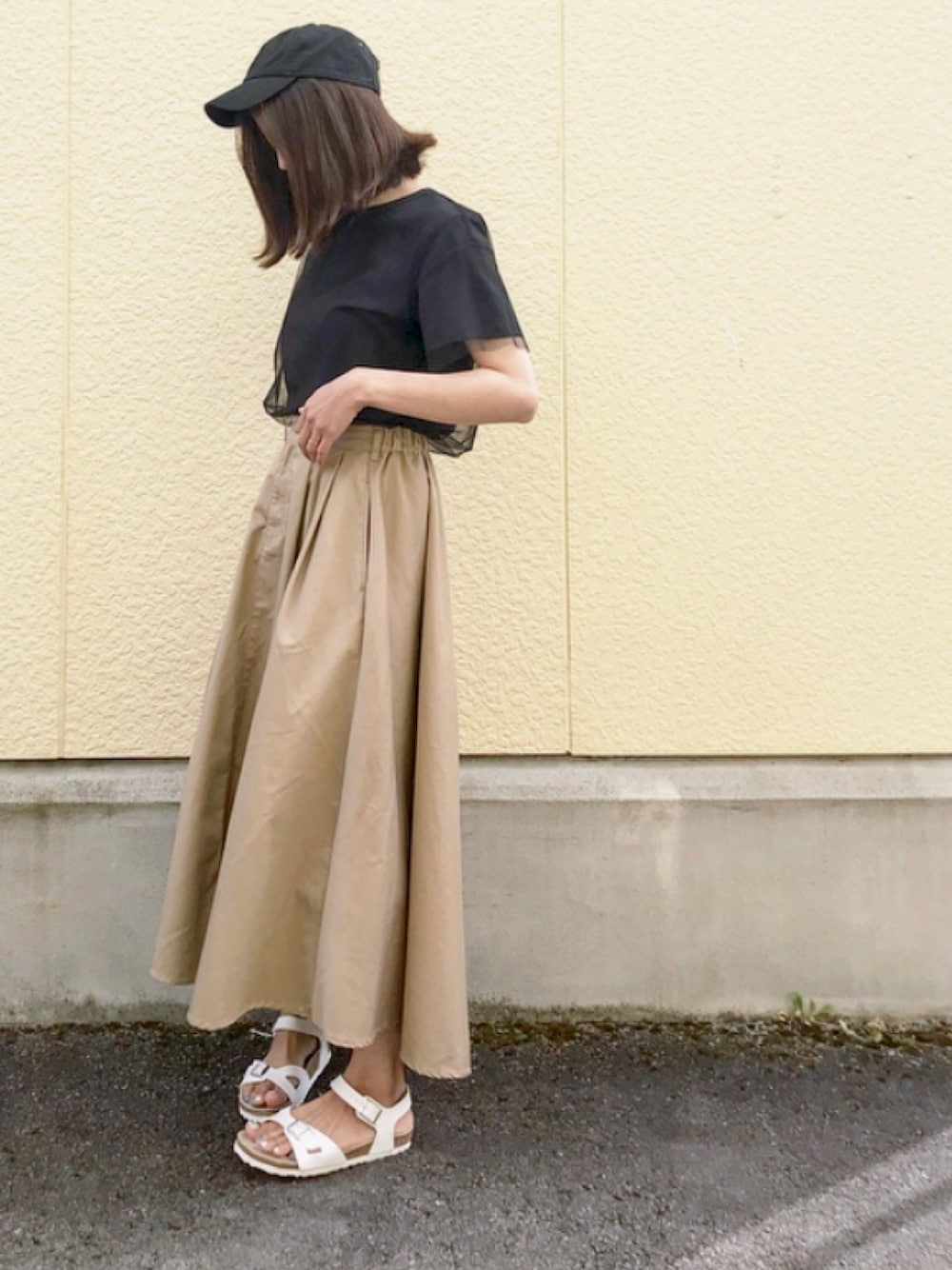 ベージュ系のスカート、ホワイト系のサンダル、ブラック系のTシャツ/カットソーを着用したレディースの春コーディネートの1枚目の写真