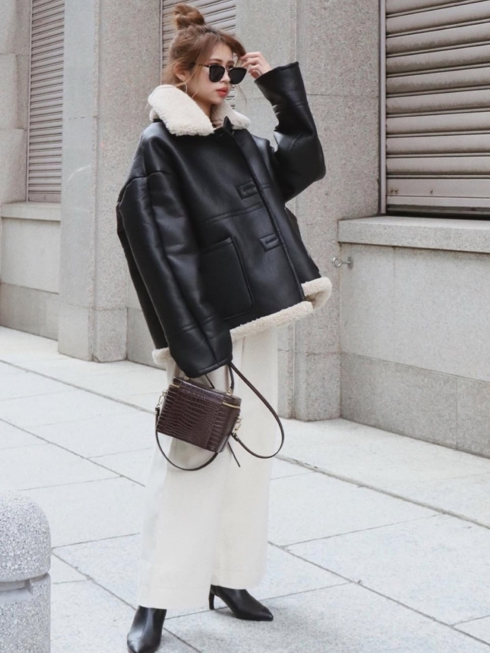 ブラック系のムートンコート、ブラウン系のバッグ、ブラック系のブーツを着用したレディースの冬コーディネートの1枚目の写真