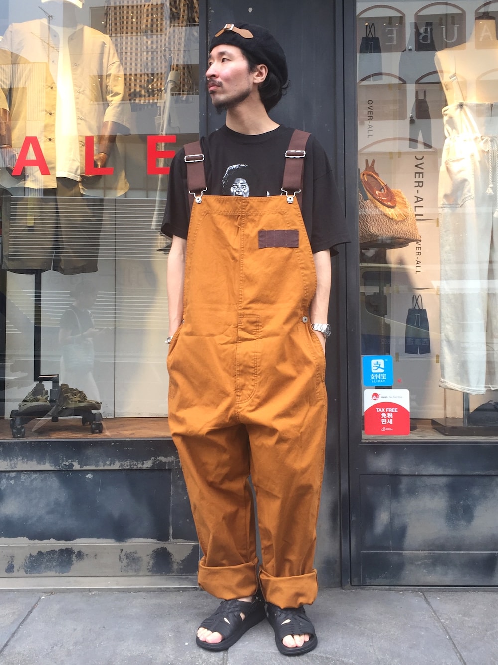 ブラック系のTシャツ/カットソー、ブラウン系のサロペット/オーバーオール、ブラック系のサンダルを着用したメンズの夏コーディネートの1枚目の写真