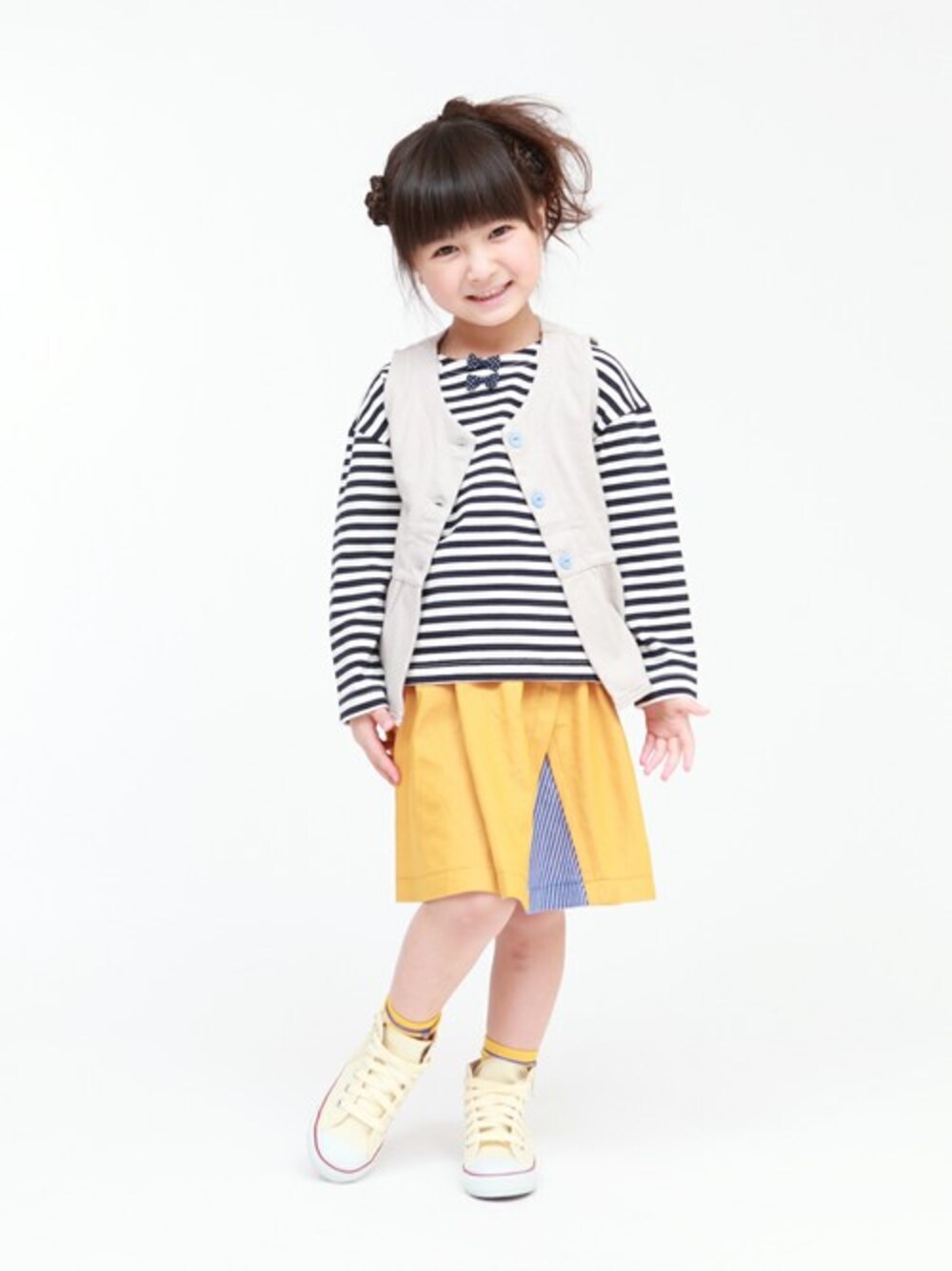 ベージュ系のベスト、ブルー系のTシャツ/カットソー、イエロー系のスカートを着用したキッズの冬コーディネートの1枚目の写真